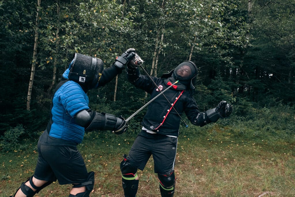 Détail sur le positionnement des mains gantées sur une poignée d'épée une main pour un contrôle optimal de l'arme adverse.